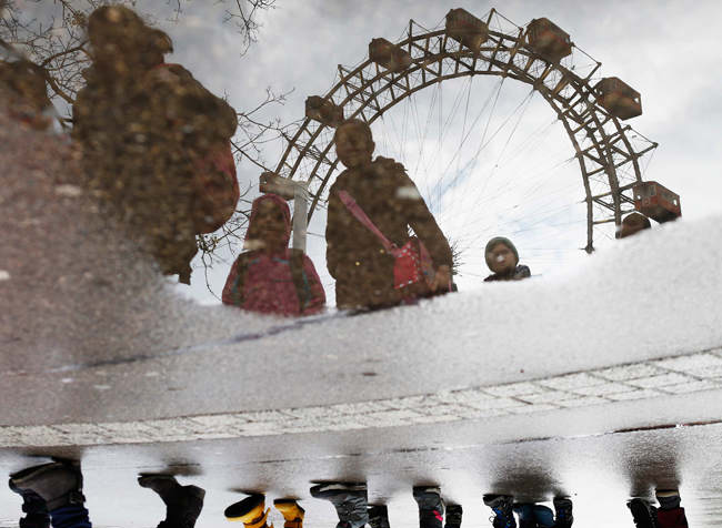 Kinder spiegeln sich in einer Pfütze vor dem Riesenrad